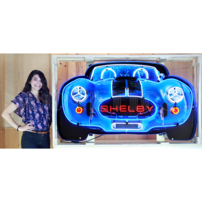 Woman standing next to neon Shelby sign.